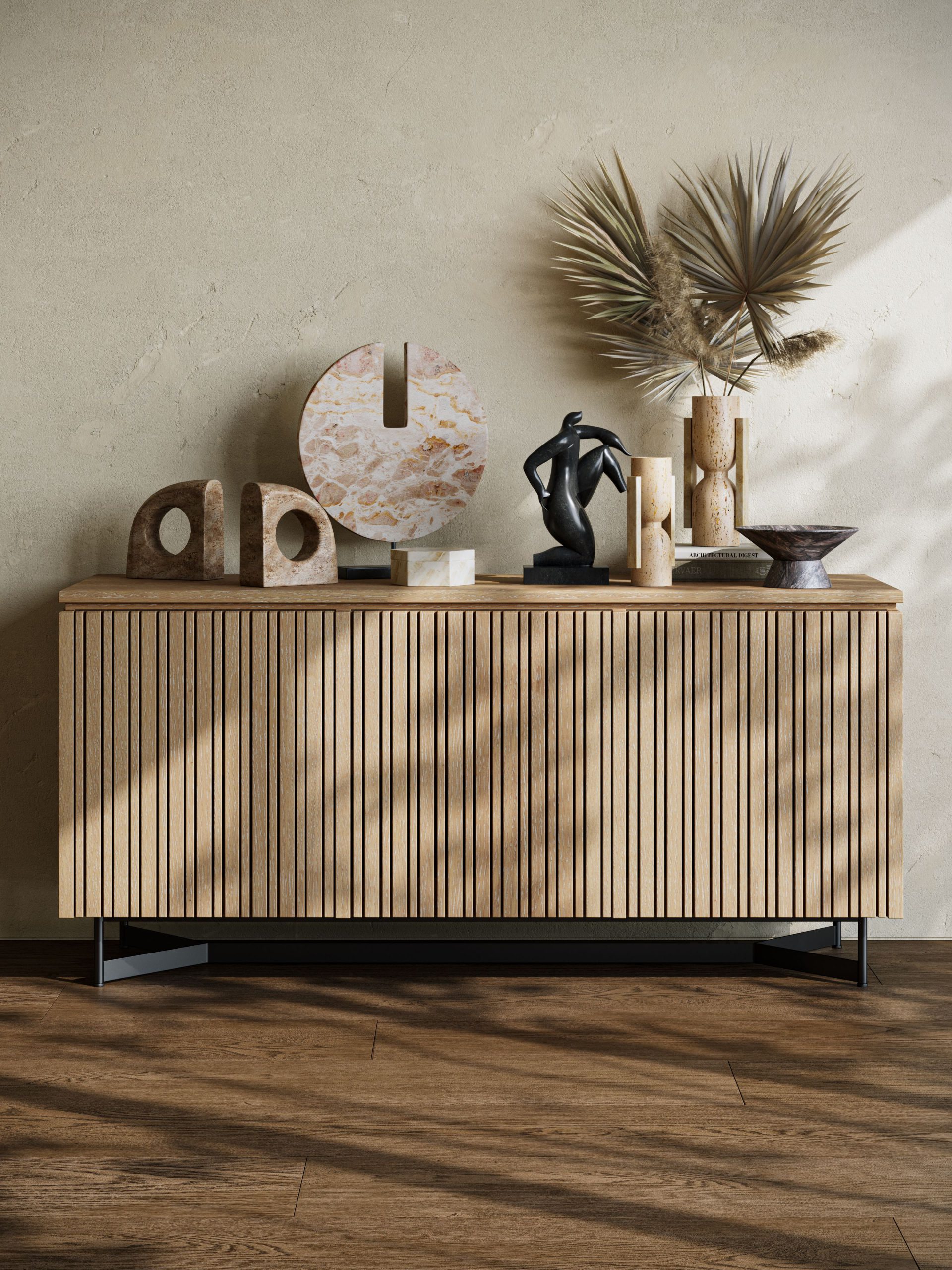 3D rendering of a fluted oak sideboard styled with abstract stone sculptures, travertine candleholders, marble bowl, and dried palm leaves against a plaster wall