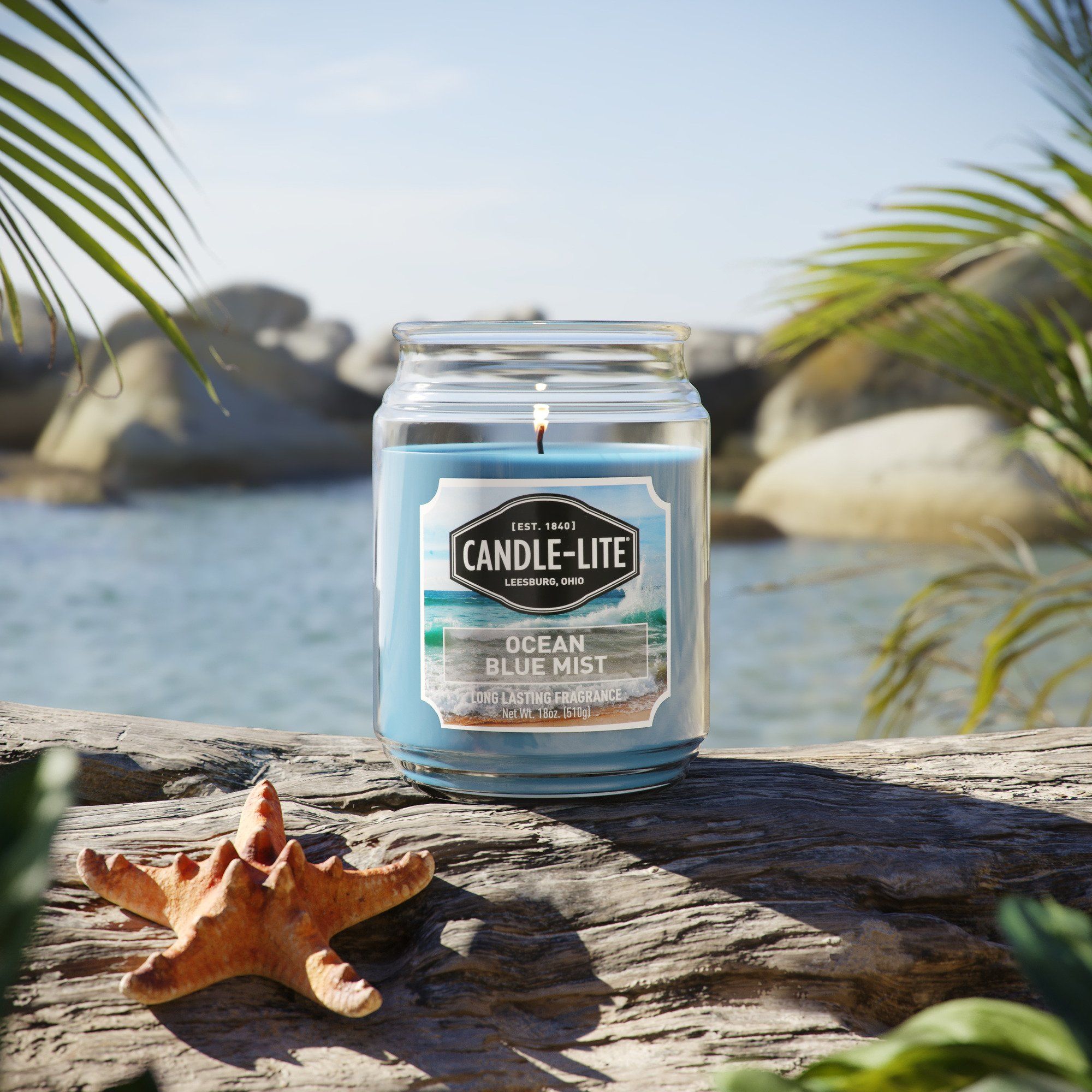 3D product rendering of Candle-Lite Ocean Blue Mist candle with beach background, showcasing photorealistic CGI visualization.